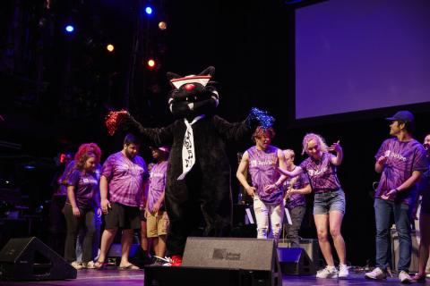 Mingus The Jazz Cat surrounding by Orientation Leaders, dancing on a stage