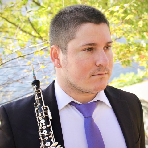 Andrew Van Der Paardt headshot; holding oboe in suit with purple tie