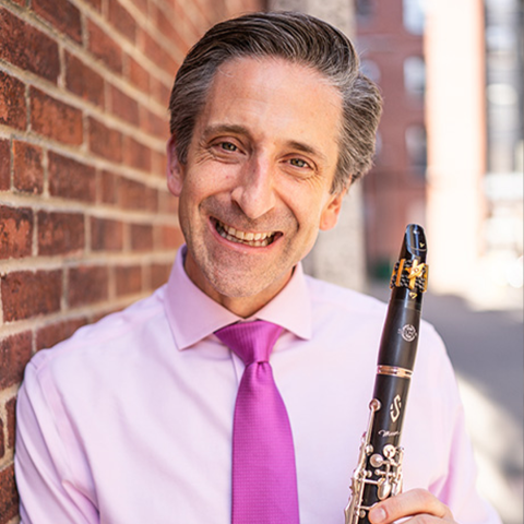 Matthew Marsit headshot, in pink shirt, pink tie, and holding clarinet.