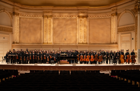 Boston Conservatory Orchestra standing side by side on Carnegie Hall stage. 