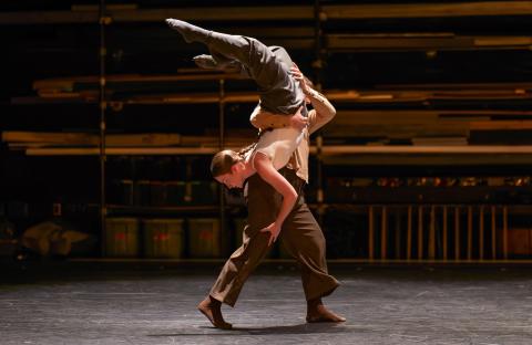 Two dancers on stage' one dancer is holding the other dancer vertically, upside down on stage.