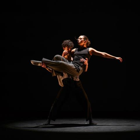 One dancer holding another dancer up on stage in a dark room
