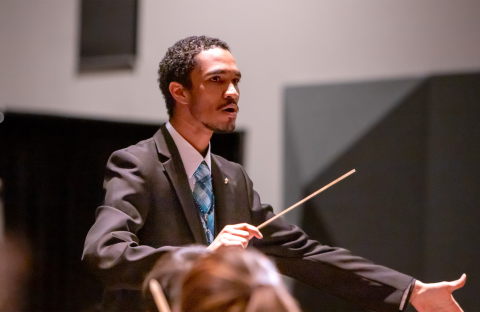 Conductor/percussionist Harold Rivas conducting an ensemble in a suit